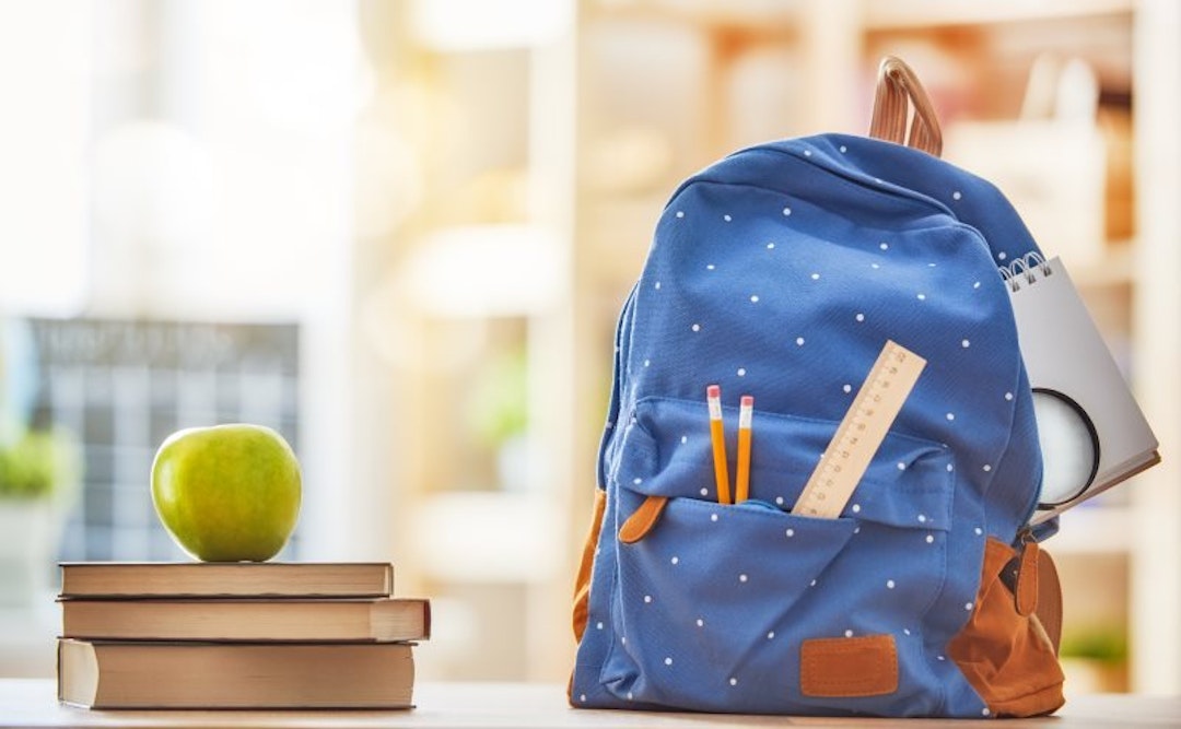 A blue backpack next to an apple stacked on top of three books.