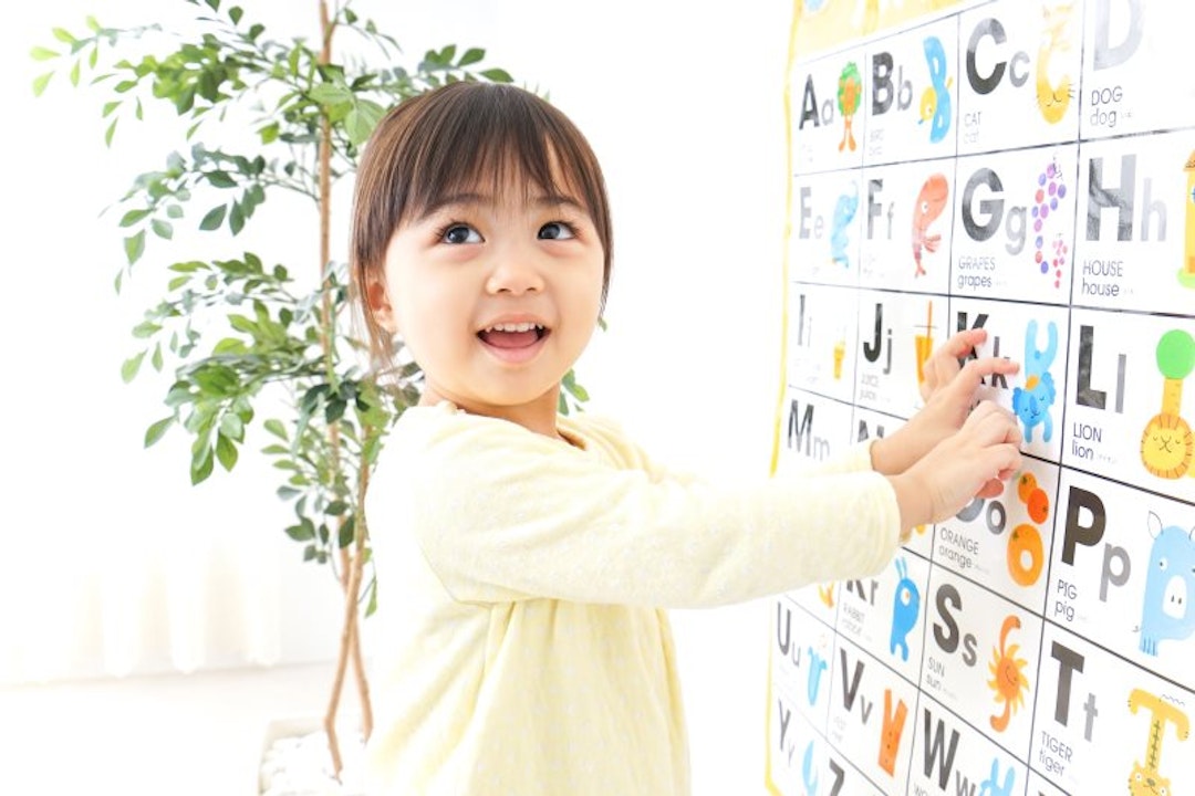 A girl pointing to a letter on an alphabet chart.