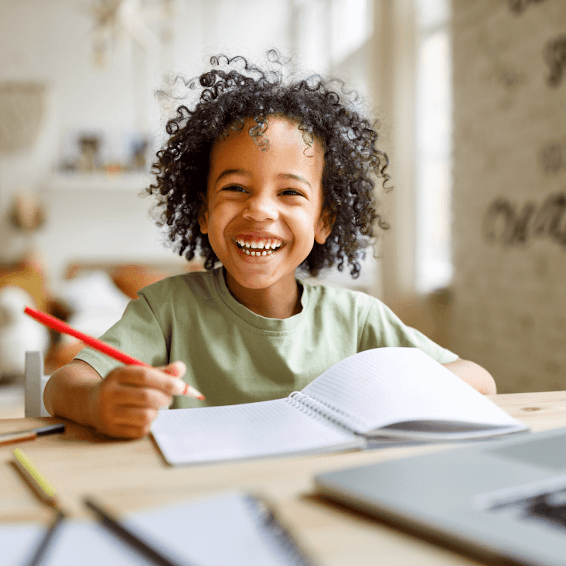 A boy smiling and writing in his notebook.