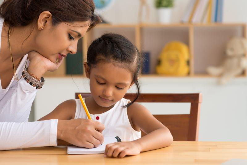 A female tutor helping a young girl as they work together in her notebook.